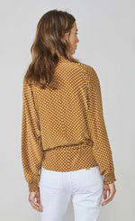 Load image into Gallery viewer, Back top half view of a woman wearing the summum 2-piece wrap blouse. This blouse has long puffy sleeves with cuffs and a relaxed fit. The wrap in this image is brown/orange with white polka dots.
