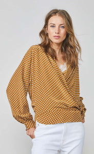Front full body view of a woman wearing the summum 2-piece wrap blouse. This blouse has long puffy sleeves with cuffs and a wrap front with a tie closure. The wrap in this image is brown/orange with white polka dots.