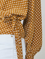 Load image into Gallery viewer, Front close up view of a woman wearing the summum 2-piece wrap blouse. This picture shows the wrap front with the tie. The wrap in this image is brown/orange with white polka dots.
