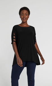 Front top half view of a woman wearing blue pants and the sympli capture tunic in black. This top has short sleeves with striped slits, a round neck, and an arched hem.