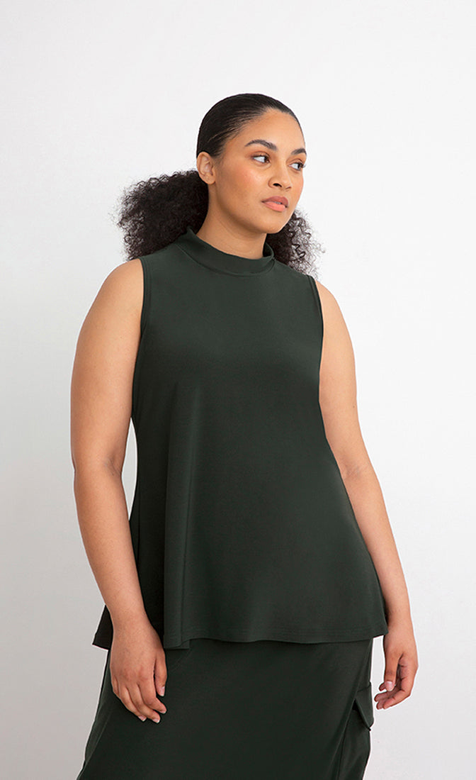 Front top half view of a woman wearing the Sympli Mock Neck Tank in the color seaweed. This top is dark green, sleeveless, and features a mock neck.