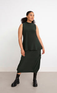 Front full body view of a woman wearing the Sympli Mock Neck Tank in the color seaweed. This top is dark green, sleeveless, and features a mock neck.
