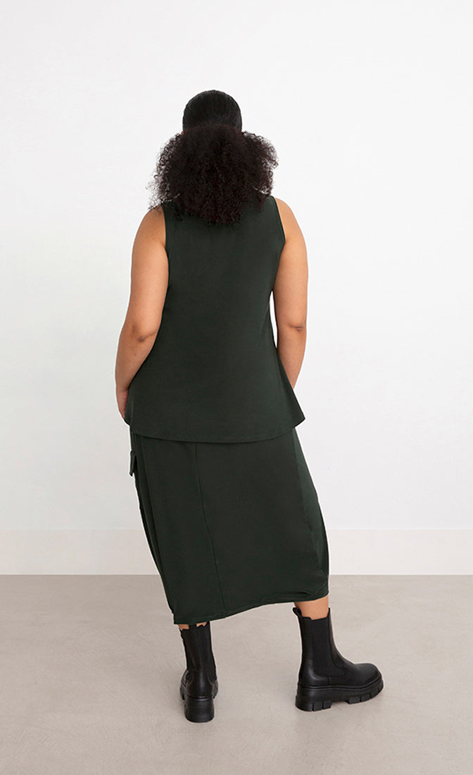 Back full body view of a woman wearing the Sympli Mock Neck Tank in the color seaweed. This top is dark green, sleeveless, and features a mock neck.