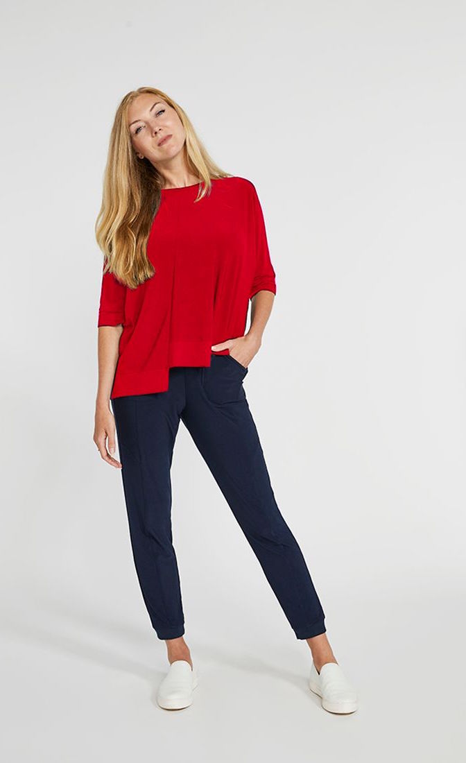 Front top full body view of a woman wearing the sympli motion boxy top in the color poppy with blue bottoms. The top has 3/4 length sleeves, a boat neck, and an asymmetrical double side-stepped hem.