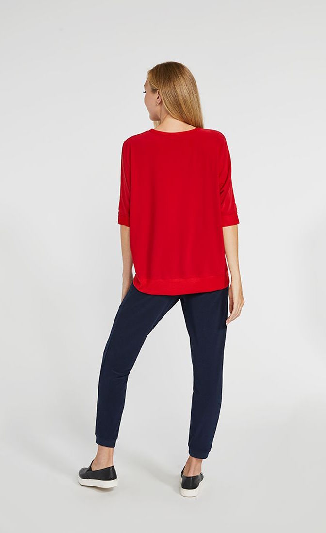 Back full body view of a woman wearing the sympli motion boxy top in the color poppy with blue bottoms. The top has 3/4 length sleeves and the back hem sits below the hips.