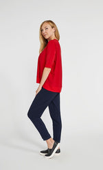 Load image into Gallery viewer, left side full body view of a woman wearing the sympli motion boxy top in the color poppy with blue bottoms. The top has 3/4 length sleeves and an asymmetrical double side-stepped hem.
