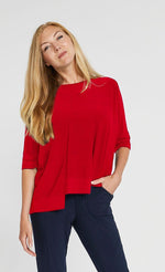 Load image into Gallery viewer, Front top half view of a woman wearing the sympli motion boxy top in the color poppy with blue bottoms. The top has 3/4 length sleeves, a boat neck, and an asymmetrical double side-stepped hem.
