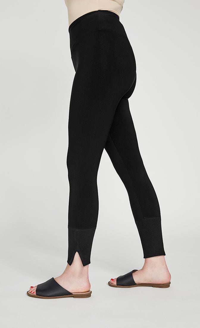 Bottom half left side view of the sympli motion trim cuff legging. This legging is black with a yoke waistband and a ribbed cuff that has a tiny side slit.