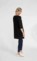 Load image into Gallery viewer, Back full body view of a woman wearing blue leggings and the sympli motion trim raglan tunic in black. This tunic has 3/4 length ribbed raglan sleeves, a ribbed hem, and long side slits.
