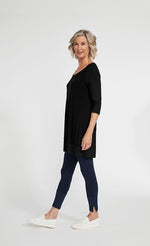Load image into Gallery viewer, Left side full body view of a woman wearing blue leggings and the sympli motion trim raglan tunic in black. This tunic has a scoop neck, 3/4 length ribbed raglan sleeves, a ribbed hem, and long side slits.
