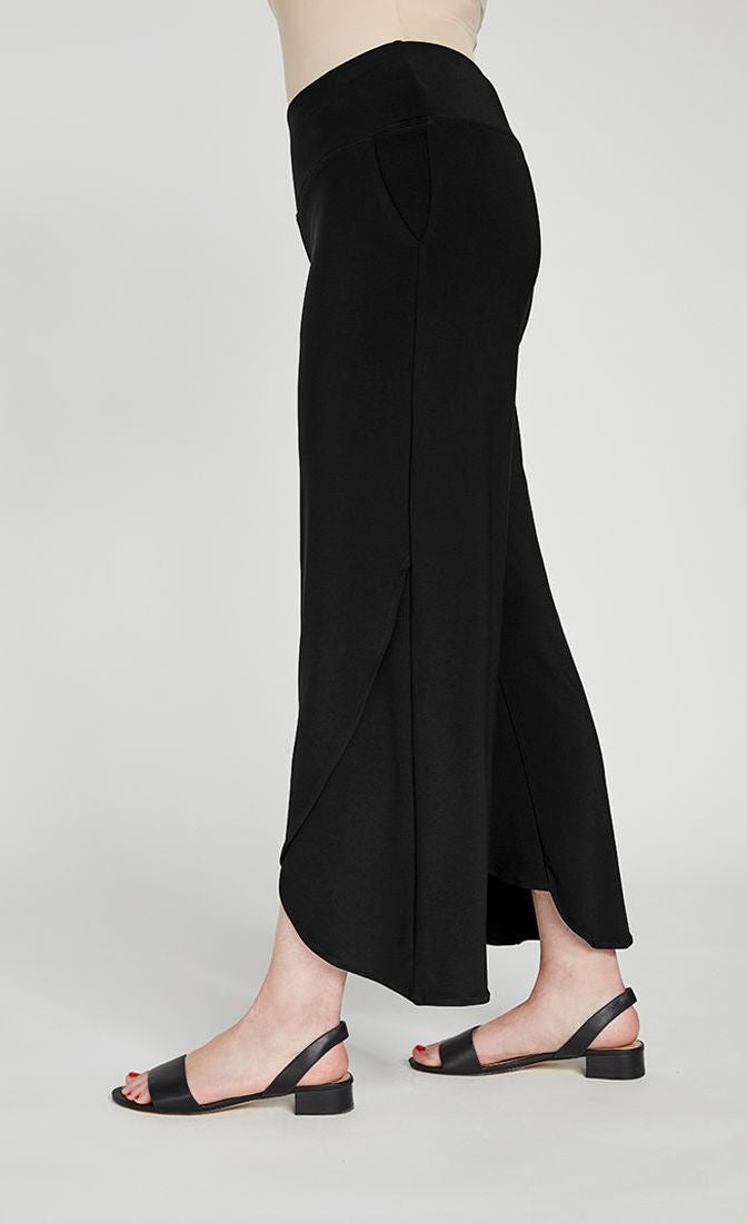 Left side bottom half view of a woman wearing the sympli narrow rapt pant. These pants are black and feature side pockets, a wide waistband, a wrapped look near the hem, and a relaxed, straight silhouette