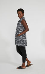 Load image into Gallery viewer, Front left side view of a woman wearing black leggings and the sympli sleeveless double take tunic. This tunic has a black and white shifted stripe print. This image shows one of the two front pockets and the collar.
