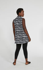 Load image into Gallery viewer, Back full body view of a woman wearing black leggings and the sympli sleeveless double take tunic. This tunic has a black and white shifted stripe print. The hem sits below the hips.
