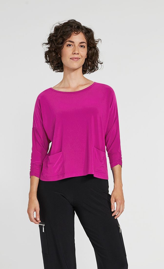 Front top half view of a woman wearing black pants and the Sympli Spark Boxy Top. This top is flamingo colored. It has two front patch pockets, a scoop neck, and 3/4 length sleeves.