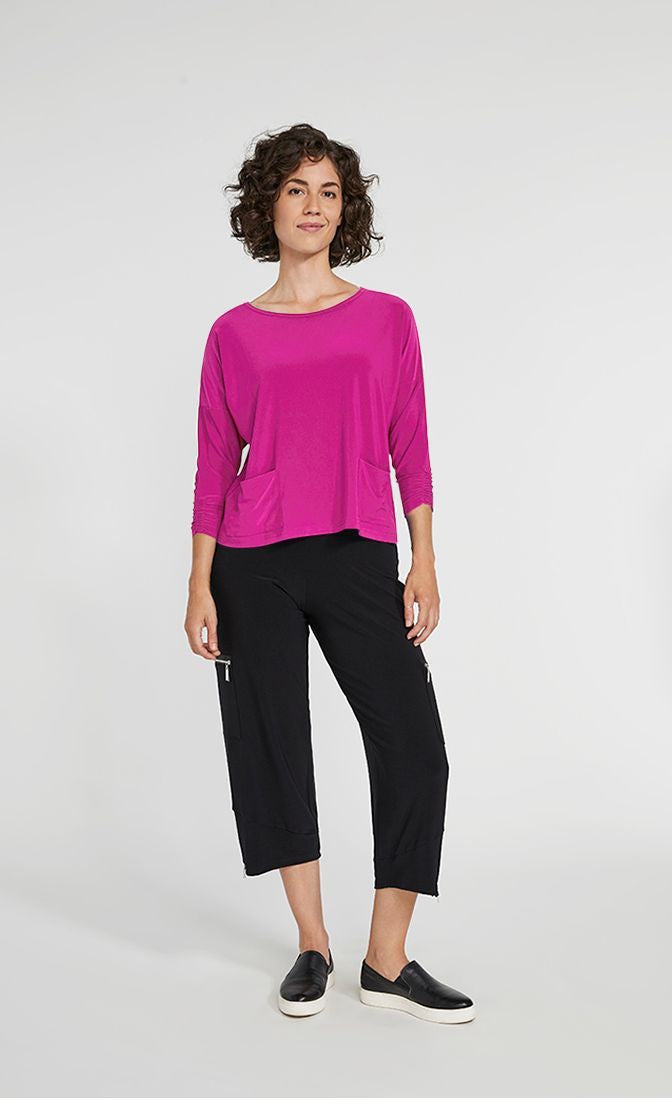 Front full body view of a woman wearing black pants and the Sympli Spark Boxy Top. This top is flamingo colored. It has two front patch pockets, a scoop neck, and 3/4 length sleeves.