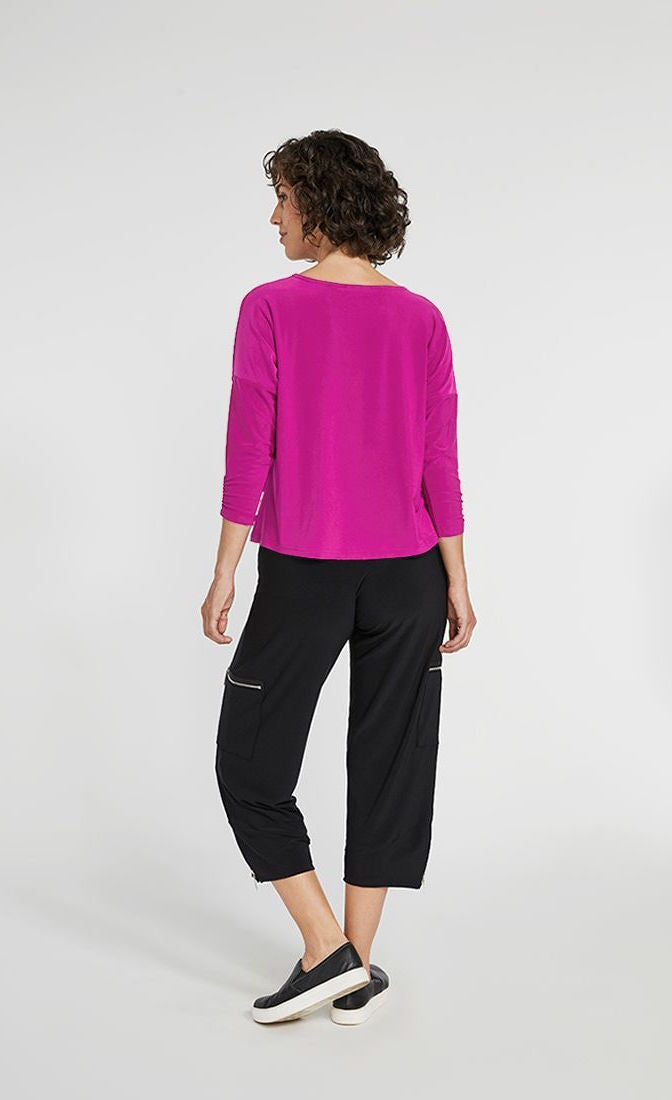 Back full body view of a woman wearing black pants and the Sympli Spark Boxy Top. This top is flamingo colored. It has 3/4 length sleeves and sits slightly above the hips.