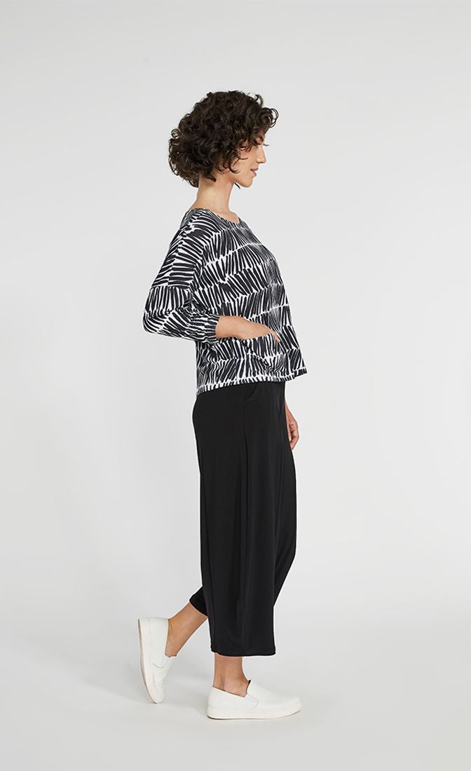 Right side full body view of a woman wearing black pants and the Sympli Spark Boxy Top. This top has black and white shifted stripes. It has two front patch pockets, a scoop neck, and 3/4 length sleeves.