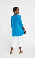 Load image into Gallery viewer, Back full body view of a woman wearing the sympli true t in the color splash. This color is a sky blue. The top has 3/4 length sleeves, a boat neck, and a flowy high-low hem with a longer back.
