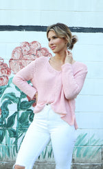 Load image into Gallery viewer, Front top half view of a woman wearing white pants and the wooden ships maui v cotton sweater in pink conch. This top has extra long sleeves, a v-neck, and a loose knit.
