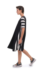 Left side, full body view of a woman wearing the alembika tekbika stripe dress. This dress is black with a striped left side and striped elbow length sleeves. The dress sits at the knees.