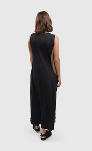 Back full body view of a woman wearing the alembika tekbika dunes wave maxi dress. This sleeveless dress is black with a wavy striped black and yellow print on the right side. The dress ends right above the ankles.