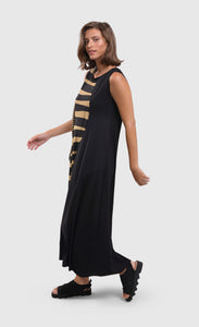 Left side full body view of a woman wearing the alembika tekbika dunes wave maxi dress. This sleeveless dress is black with a wavy striped black and yellow print on the right side. The dress also has a single front draped pocket on the right side. 