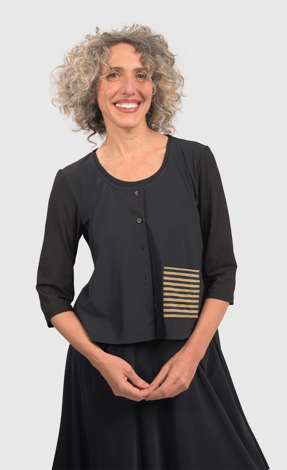 Front top half view of a woman wearing black pants and the alembika tekbika dune crop jacket. This jacket is black with a single left sided front pocket that is striped black and yellow. The jacket has 3/4 length sleeves and a button down front.