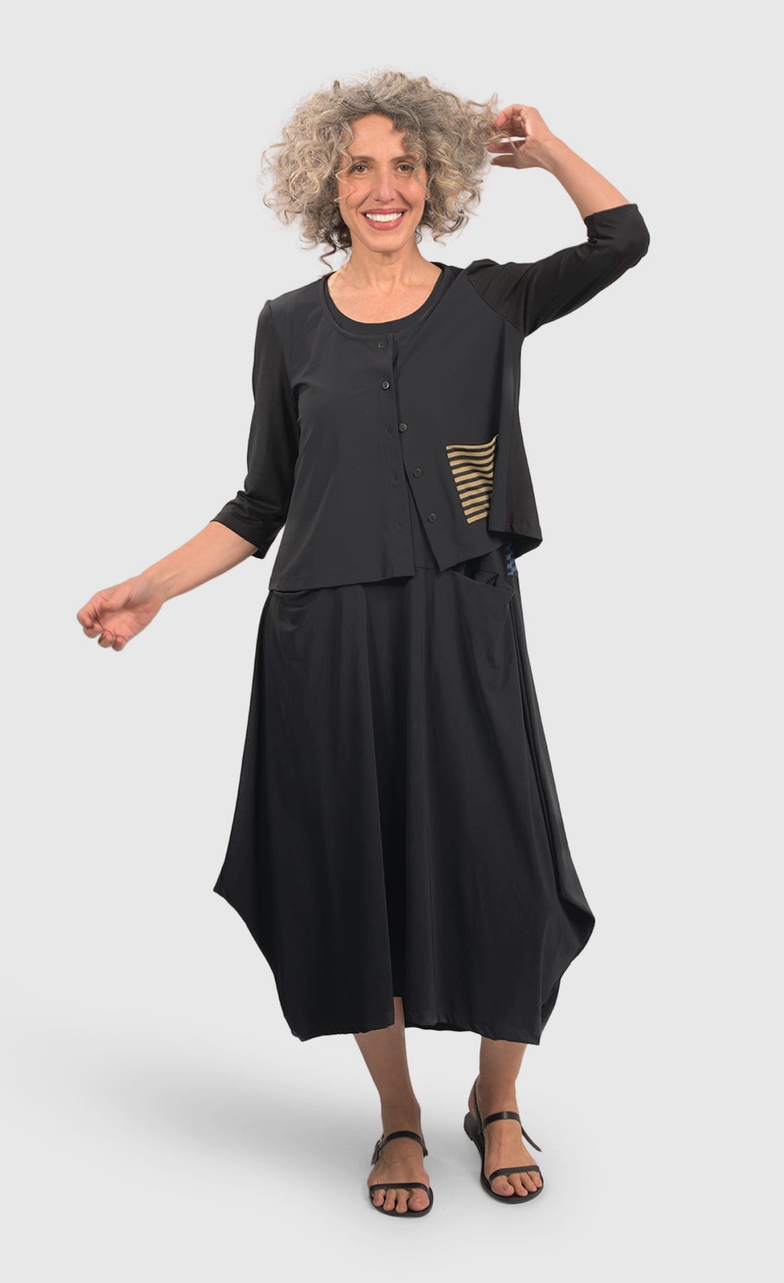 Front full body view of a woman wearing black pants and the alembika tekbika dune crop jacket. This jacket is black with a single left sided front pocket that is striped black and yellow. The jacket has 3/4 length sleeves and a button down front.
