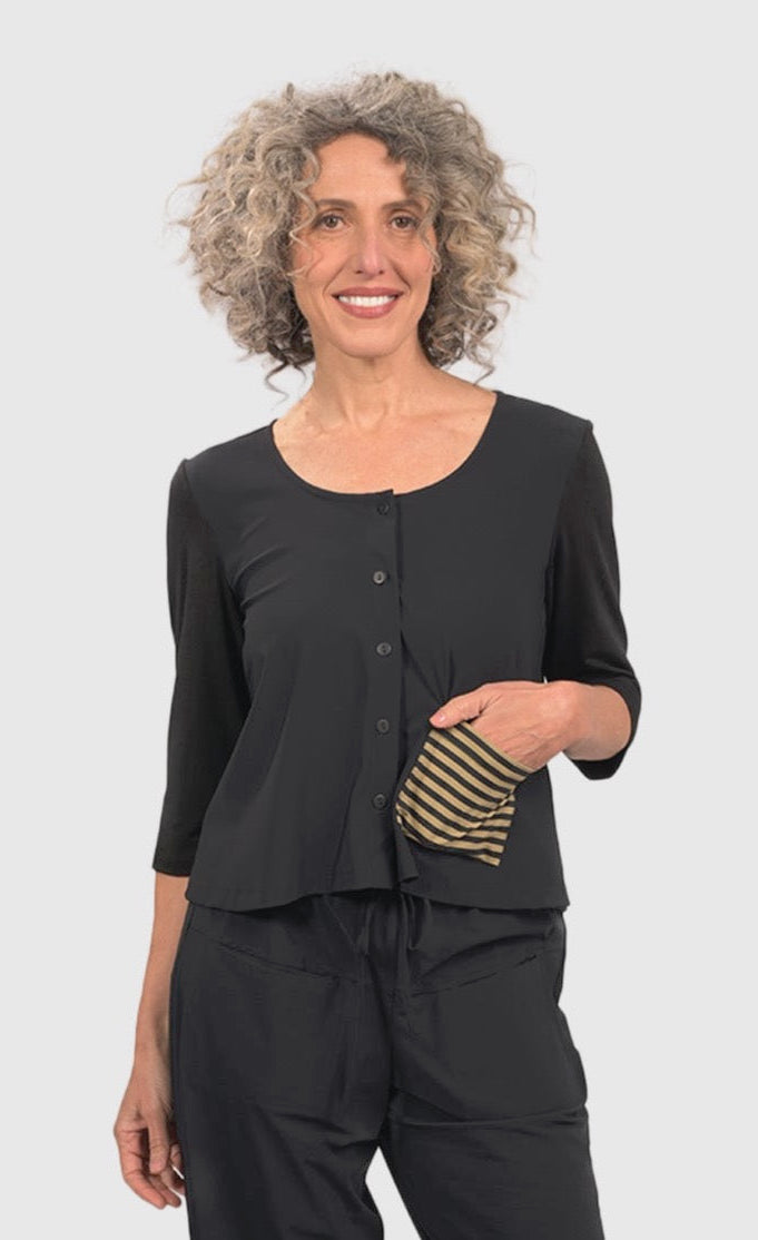 Front top half view of a woman wearing black pants and the alembika tekbika dune crop jacket. This jacket is black with a single left sided front pocket that is striped black and yellow. The jacket has 3/4 length sleeves and a button down front.