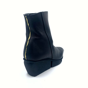 Outer back side view of the trippen flaw boot in black waw. The back of this squared-toe boot has a cracked gold seam. The boot has a black wedged sole.
