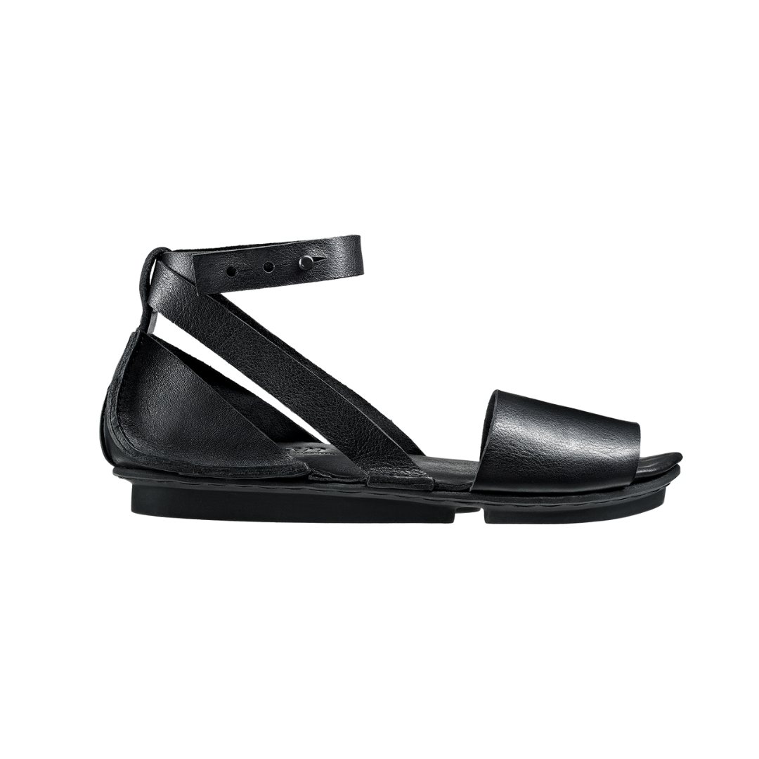 Outer view of the trippen iris sandal in black. This flat sandal has a wide strap over the toes, leather that covers the heel, and an ankle strap that criss crosses and attaches to the sole on both sides of the shoe.