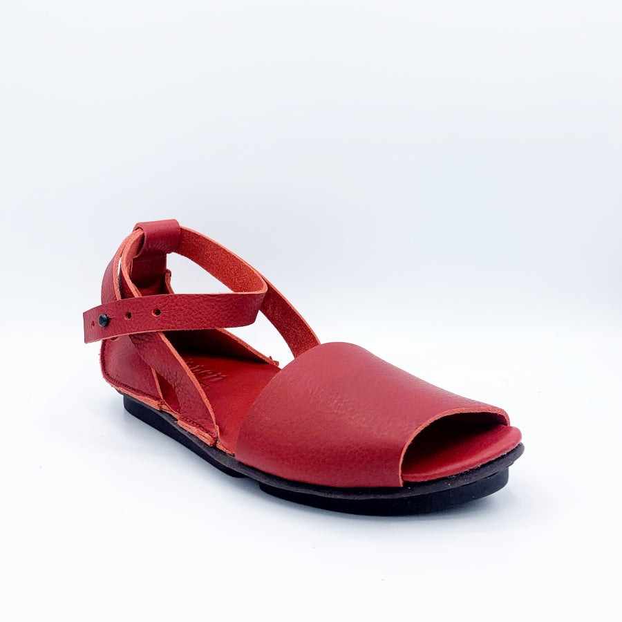 Outer front view of the trippen iris sandal in red. This flat sandal has a wide strap over the toes, leather that covers the heel, and an ankle strap that criss crosses and attaches to the sole on both sides of the shoe.