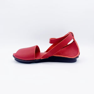 Inner view of the trippen iris sandal in red. This flat sandal has a wide strap over the toes, leather that covers the heel, and an ankle strap that criss crosses and attaches to the sole on both sides of the shoe.