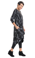 Load image into Gallery viewer, Right side full body view of a woman wearing the tulip karma dress in black with a grey airbrush print. The dress has long sleeves, a gathered knot in the front, and pockets.

