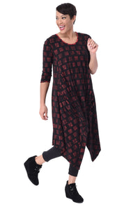 Front full body view of a woman wearing the tulip lexi tunic dress in the black with cherry cracker print all over it. This dress has long sleeves, a round neck, and a pointed hem.