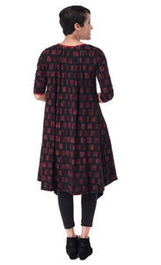 Back full body view of a woman wearing the tulip lexi tunic dress in black with cherry cracker print all over it. This dress has long sleeves and inverted pleats on the back