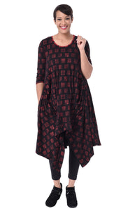 Front full body view of a woman wearing the tulip lexi tunic dress in black with cherry cracker print all over it. This dress has long sleeves, a round neck, and a pointed hem.