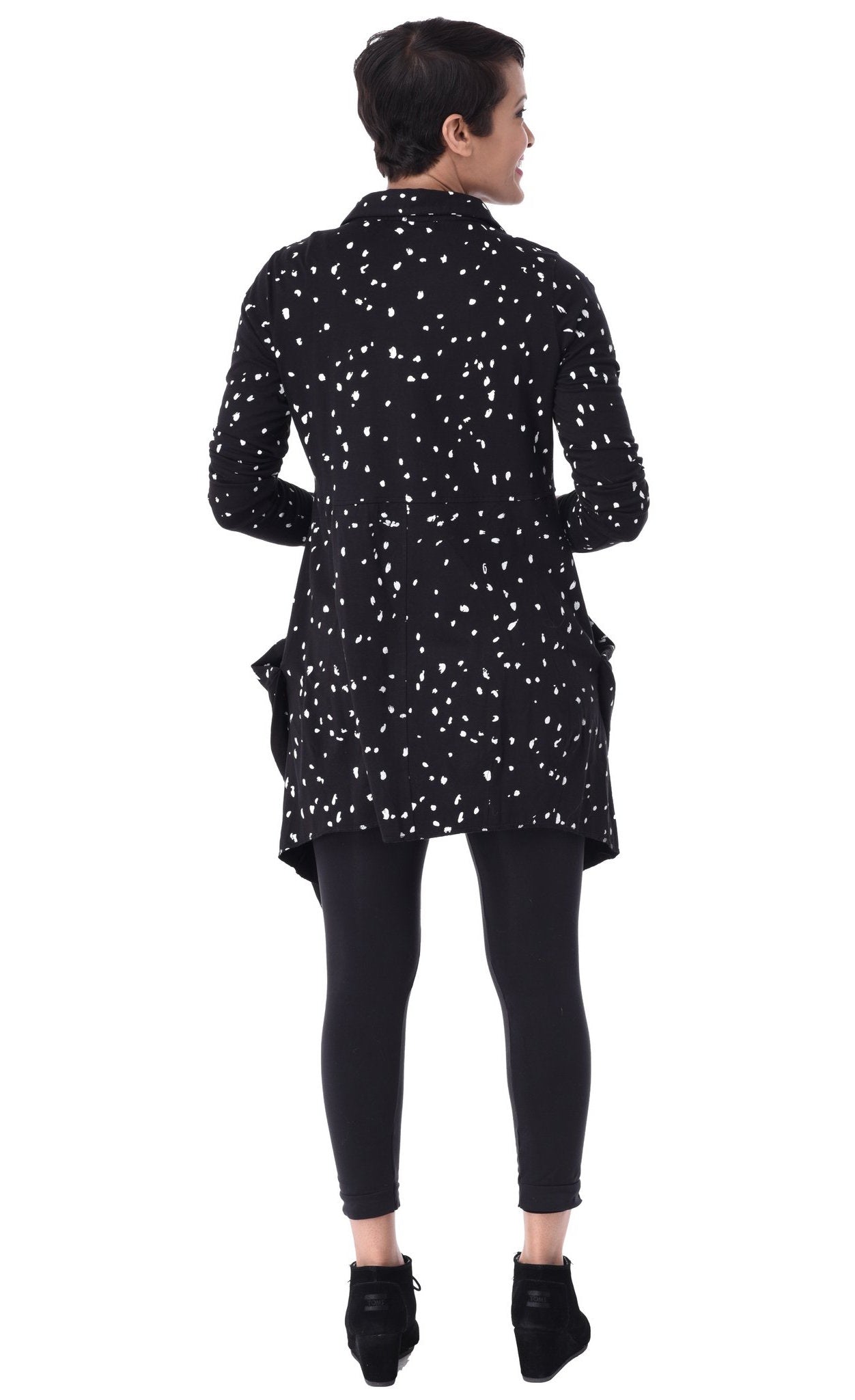 Back full body view of a woman wearing the tulip macy raindrop jacket. This jacket is black with white raindrops all over it. The sleeves are long and the top has a shorter back that sits below the hips.