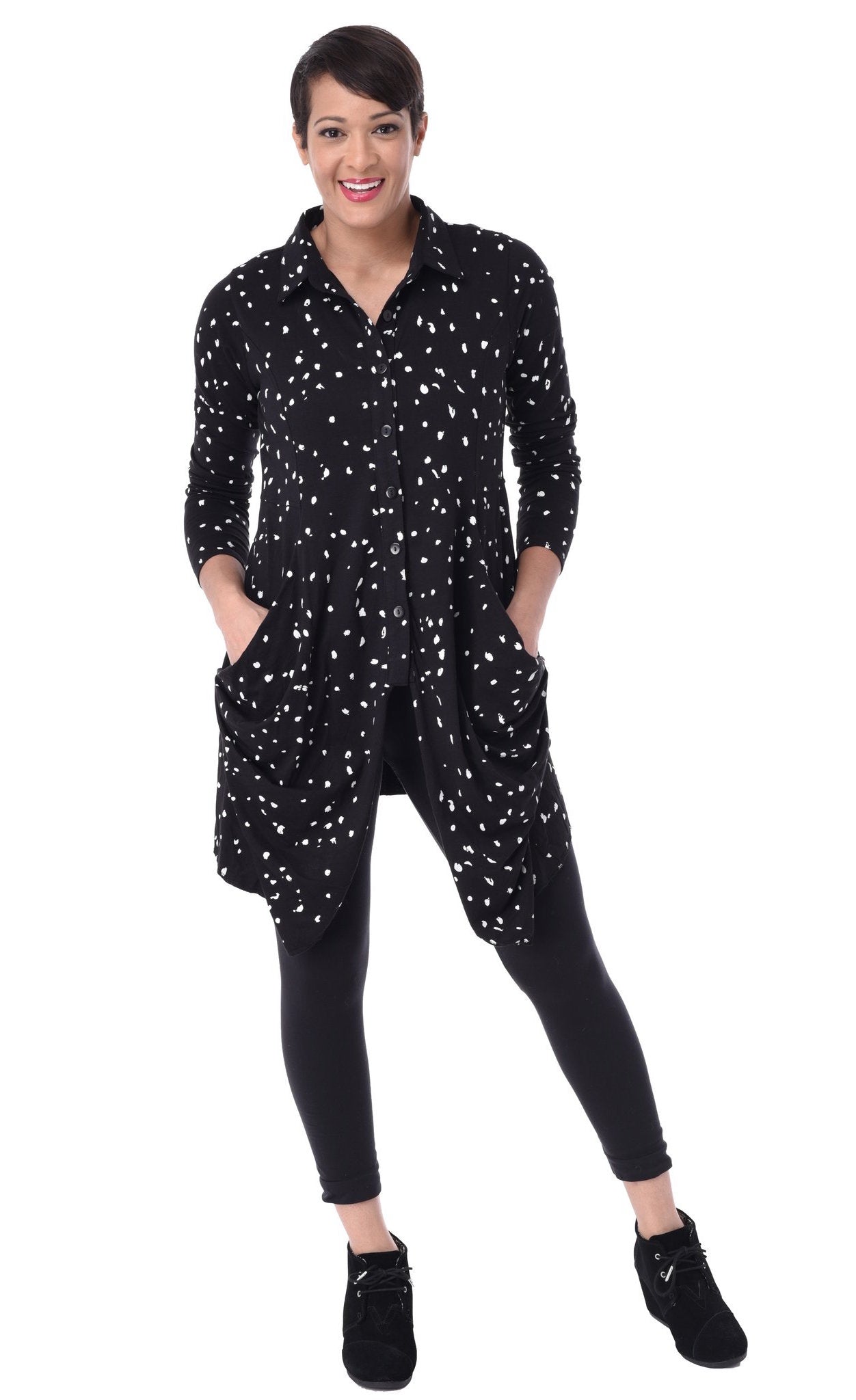 Front full body view of a woman wearing the tulip macy raindrop jacket. This jacket is black with white raindrops all over it. The sleeves are long and the top has a button down front with two draped pocket panels on each side.