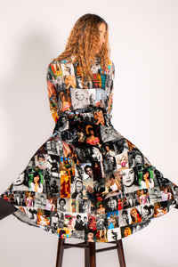Front full body view of a woman sitting on a stool and wearing the long unbreakable evolution gio skirt in the black and white print with hints of colors. This print features different images of stars from the 50s and 60s. 