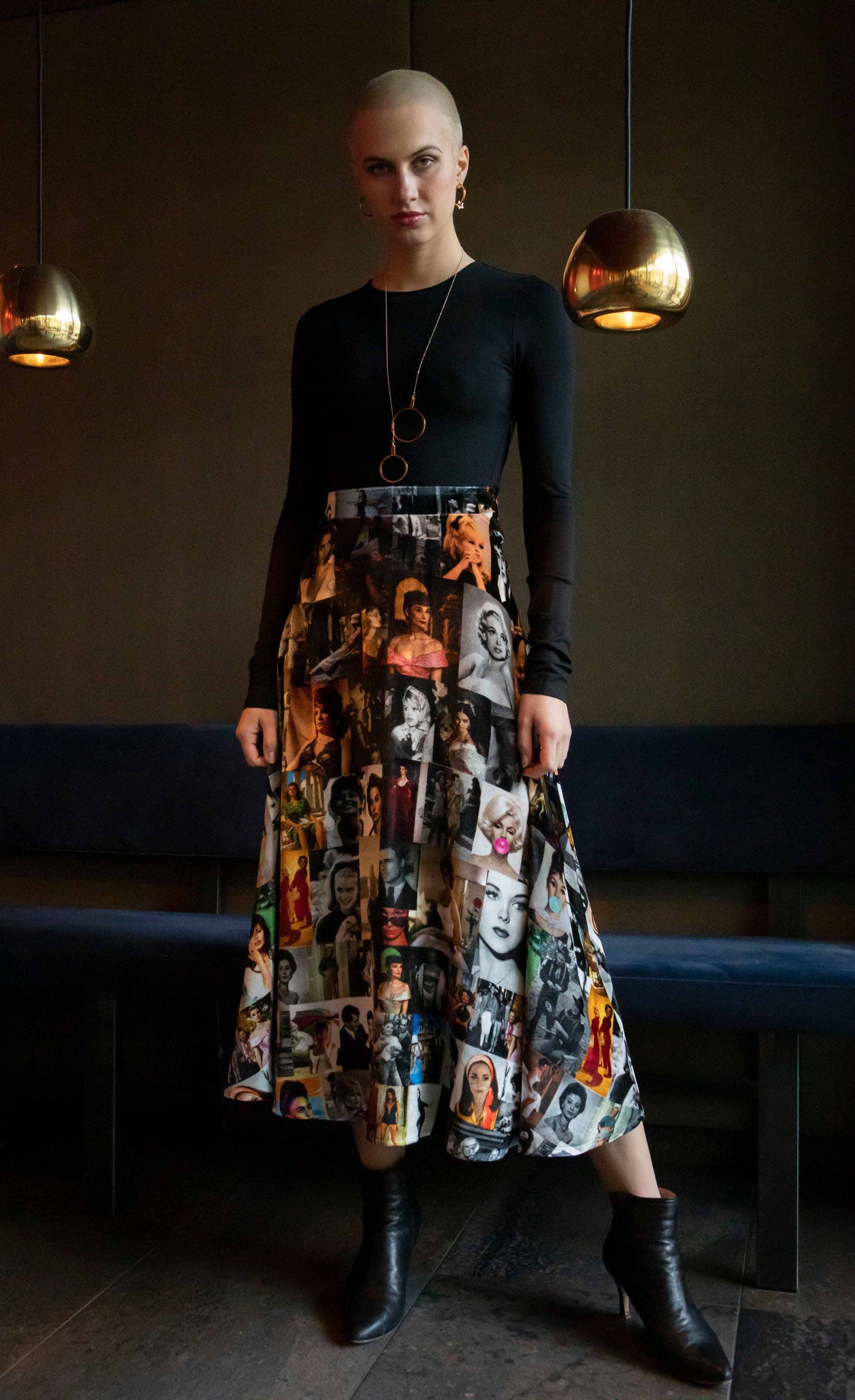 Front full body view of a woman wearing the long unbreakable evolution gio skirt in the black and white print with hints of colors. This print features different images of stars from the 50s and 60s.