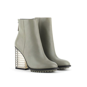 Outer and inner side view of a pair of the united nude hi rise bootie. This bootie is grey with a glass like see-through, block shaped high heel. The bootie is an ankle bootie with a back zipper.