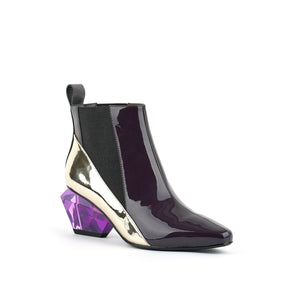 Front outer side view of the united nude jacky h bootie. This bootie sits at the ankles. The top of the shoe is midnight brown. The bottom part of the shoe is silver. This bootie has elastic sides and a purple glass like heel.