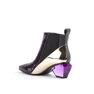 Inner back side view of the united nude jacky h bootie. This bootie sits at the ankles. The top of the shoe is midnight brown. The bottom part of the shoe is silver. This bootie has elastic sides and a purple glass like heel.