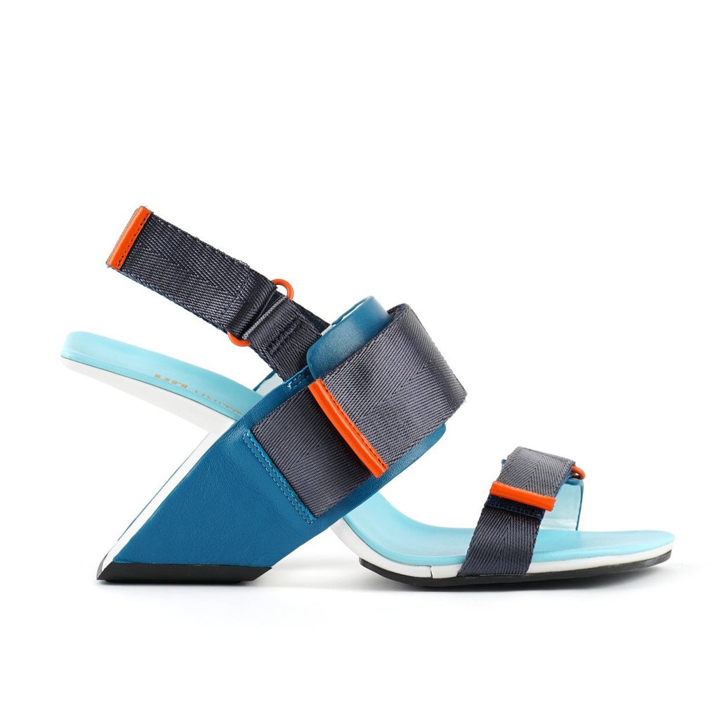 Outer view of the united nude loop run high heel sandal. This sandal is blue with a black back strap, a black strap over the instep, and a black strap over the toes.