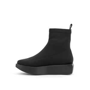 Inner side view of the united nude wa bootie lo. This bootie is black and minimal. It has a sock-like appearance with a black platform sole.