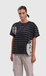 Load image into Gallery viewer, Front top half view of a woman wearing the alembika urban stripe moon boxy tee. This top has grey and black striping with two circular patches of a white fabric that have a scribble print on them. The top has a crew neck, a wide silhouette, and short sleeves.
