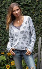 Load image into Gallery viewer, Front top half view of a woman wearing jeans and the wooden ships distressed leopard sweater. This sweater is grey with dark grey leopard print on the front. The sweater has a v-neck and is distressed.

