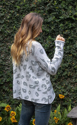 Load image into Gallery viewer, Right side top half view of a woman wearing jeans and the wooden ships distressed leopard sweater. This sweater is grey with dark grey leopard print on the front. The sweater is also distressed
