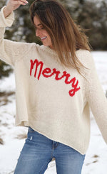 Load image into Gallery viewer, Front top half view of a woman wearing the wooden ship merry chunky crew sweater in the color alabaster/ginger. This sweater is white with the word merry written in red cursive on the front.
